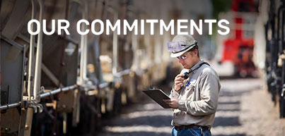 Image of ERCO working on a railroad track alongside a train looking at a clipboard. A text overlay reads "OUR COMMITMENTS"