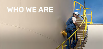 Image of a worker wearing a white hard hat walking up a yellow staircase that runs up and down a large white tank. Text overlay reads "WHO WE ARE"