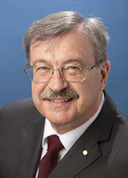 Male executive members of ERCO Worldwide wearing a gray suit with a white shirt and dark red tie. He has gray hair, a mustache, and is wearing glasses.