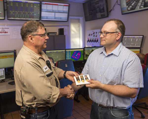 Two ERCO workers both wearing glasses shake hands in a control room while one hands a card to the other