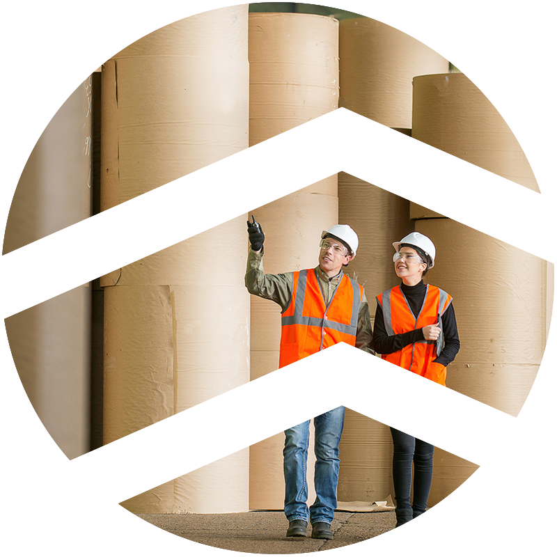 Two workers wearing safety helmets and orange vests stand in front of industrial rolls of paper. Two white V shaped lines pointing upward are overlaid on the circular image to signify the ERCO brand.