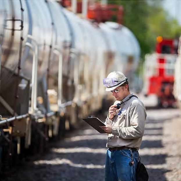 ERCO worker reviewing plans on a clipboard in front of a train on railroad tracks